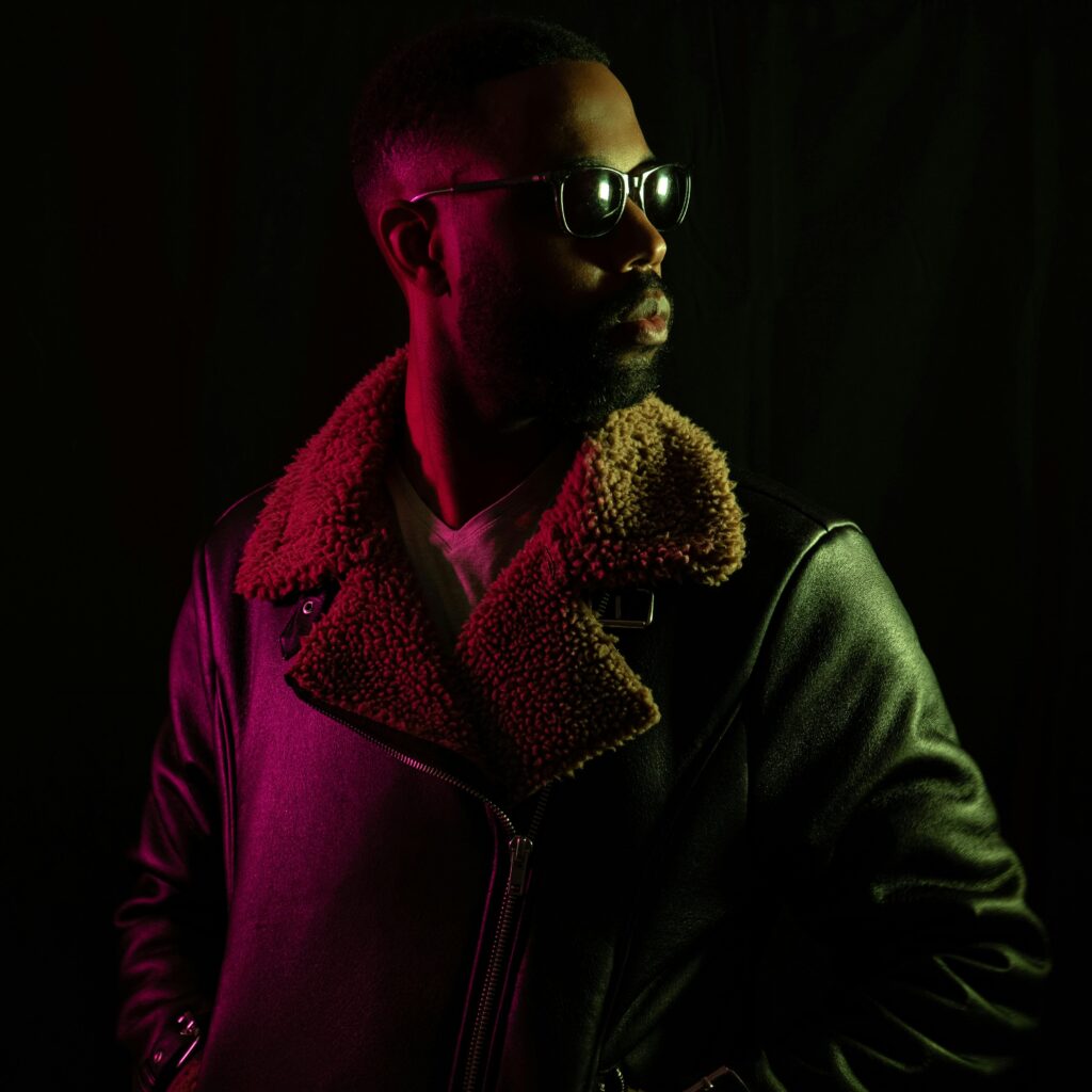 African American man in leather jacket and sunglasses with moody lighting in studio.