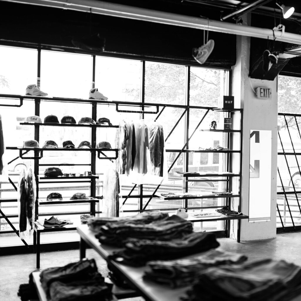 Black and white photo of a retail clothing store interior with hats, shirts, and racks.